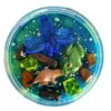 Rond doosje gevuld met groene en blauwe sensorische klei, versierd met een plastic libelle, bever, kikker en kleurrijke steentjes, boomstammen en glitter – een zoemende sloot- of rivierzijde in miniatuurformaat.