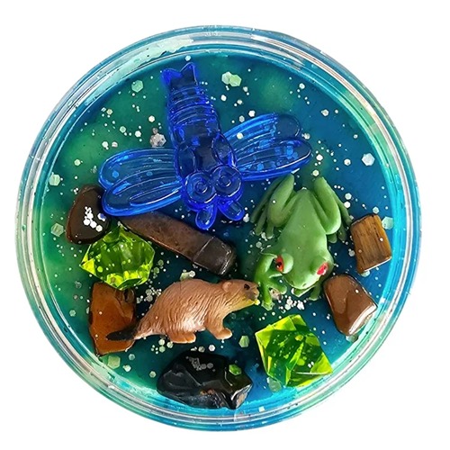 Sloot Rond doosje gevuld met groene en blauwe sensorische klei, versierd met een plastic libelle, bever, kikker en kleurrijke steentjes, boomstammen en glitter – een zoemende sloot- of rivierzijde in miniatuurformaat.