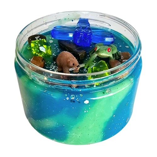 rivier, river Rond doosje gevuld met groene en blauwe sensorische klei, versierd met een plastic libelle, bever, kikker en kleurrijke steentjes, boomstam en glitte – een zoemende sloot- of rivierzijde in miniatuurformaat.